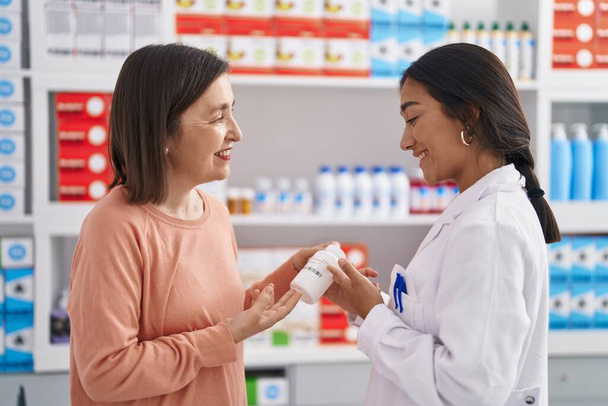 Two women pharmacist and customer holding pills bottle at pharmacy - Foto, afbeelding