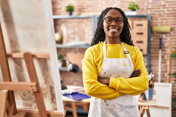 Αφρο-αμερικανίδα καλλιτέχνης χαμογελώντας αυτοπεποίθηση στέκεται με τα χέρια σταυρωμένα χειρονομία στο στούντιο τέχνης - Φωτογραφία, εικόνα