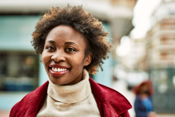 Belle femme afro-américaine d'affaires avec les cheveux afro souriant heureux et confiant en plein air à la ville - Photo, image
