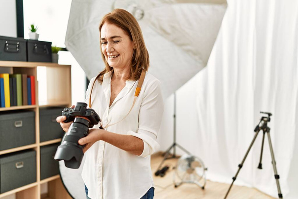 Середньовічна біла жінка-фотограф посміхається впевнено тримає професійну камеру в фотостудії
 - Фото, зображення