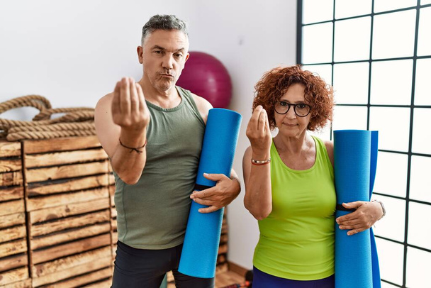 Middle age couple holding yoga mat doing italian gesture with hand and fingers confident expression  - Photo, Image