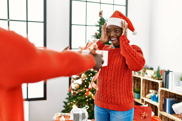 African man surprising his girlfriend with christmas gift at home. - Photo, Image