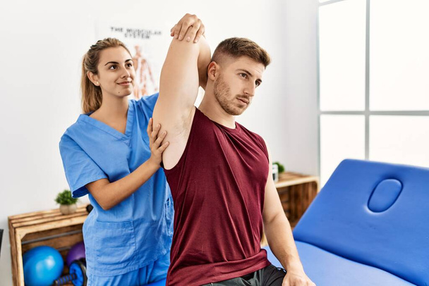 Mujer fisioterapeuta hispana joven hace tratamiento de rehabilitación del brazo al hombre en la clínica. - Foto, imagen
