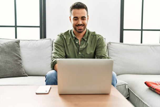 Joven hombre hispano sonriendo confiado usando portátil en casa - Foto, imagen