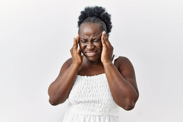 Jonge Afrikaanse vrouw die over een witte geïsoleerde achtergrond staat met hand op hoofd, hoofdpijn door stress. lijden aan migraine.  - Foto, afbeelding