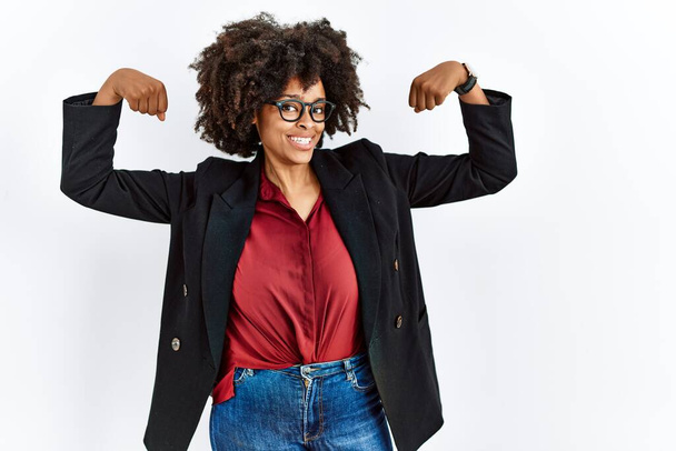 Africano mulher americana com cabelo afro vestindo jaqueta de negócios e óculos mostrando músculos braços sorrindo orgulhoso. conceito de aptidão.  - Foto, Imagem