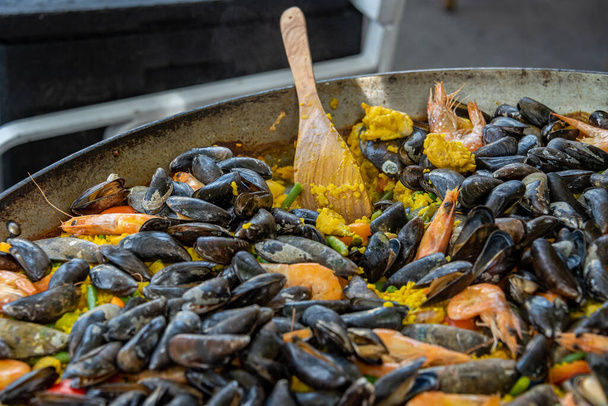 Traditionelle spanische Paella mit Reis, Muscheln, Garnelen in einer großen Pfanne im Freien. Blick von oben schräg, flache Lage - Foto, Bild