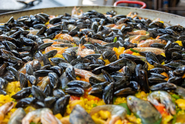 Traditional Spanish paella with rice, mussels, shrimp in a large outdoor pan. View from oblique above, flat layer - Photo, Image