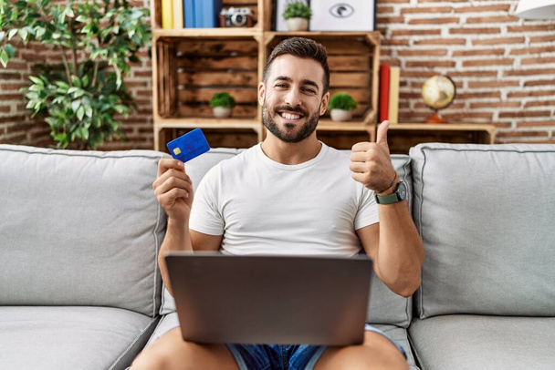 オンラインショッピングを行うハンサムなヒスパニック系の男性クレジットカードを保持笑顔幸せと肯定的な、親指を行う優れた承認サイン  - 写真・画像