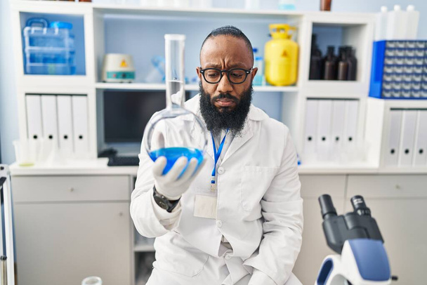 Νεαρός Αφροαμερικάνος άνδρας φορώντας στολή επιστήμονα κρατώντας δοκιμαστικό σωλήνα στο εργαστήριο - Φωτογραφία, εικόνα