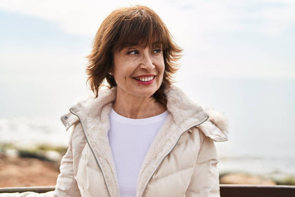 Middle age woman smiling confident looking to the side at seaside - Photo, Image