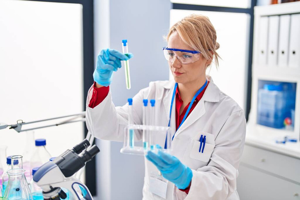 Nuori blondi nainen tiedemies, jolla on koeputkia laboratoriossa - Valokuva, kuva