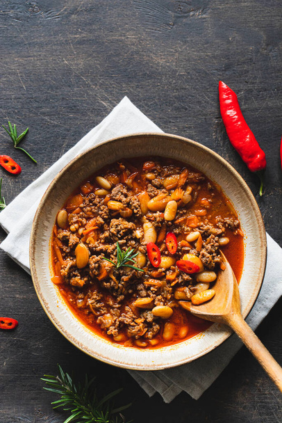 Chili Con Carne in bowl on dark background. Mexican cuisine. chili con carne - minced meat and vegetables stew in tomato sauce. Top view - Photo, Image