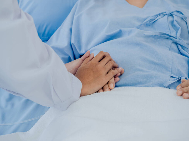 病院のベッドに生理食塩水のホースが横たわっているライトブルーのドレスで高齢女性患者の手に白いスーツのクローズアップ女性医師が開催され、患者の概念を奨励. - 写真・画像