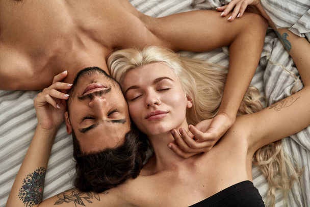 Cropped view of young beautiful multiethnic couple sleeping on bed at home. Caucasian girl and middle eastern man with closed eyes touching each other. Domestic lifestyle. Closeness - Fotoğraf, Görsel