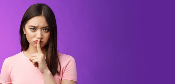 Close-up offended serious-looking upset asian young girl frowning cannot focus disturbed loud conversation, hush stare camera unsatisfied, show shush sign press finger lips, purple background. - Photo, Image