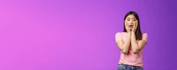 Concerned shocked timid insecure asian woman, feel pitty, shame hearing shocking news, grab face sorry for friend, gasping, opened mouth upset, sighing distressed, stand purple background. - Photo, Image