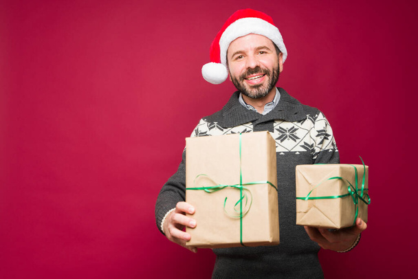 Возбужденный привлекательный мужчина несет и получает много рождественских подарков во время празднования праздников - Фото, изображение