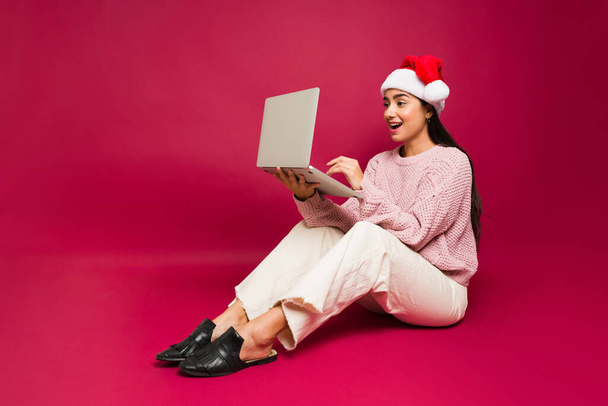 Meglepett gyönyörű nő keres izgatott az ünnep eladó, miközben csinál online vásárlás karácsonyi ajándékok - Fotó, kép