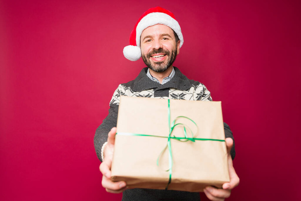 Very happy man making eye contact giving a christmas present to family or friends and celebrating the holidays - Фото, изображение