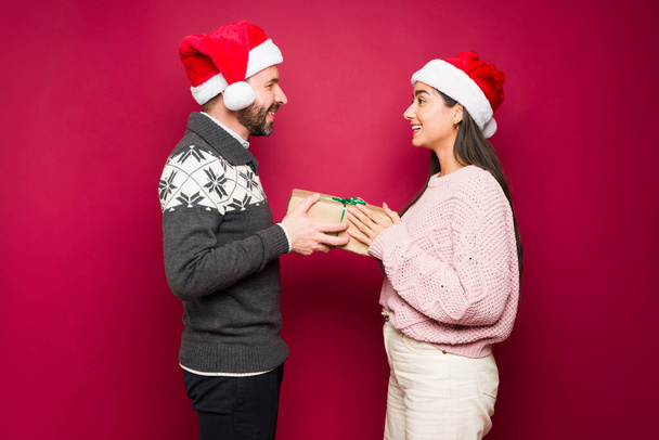 Attractive latin man surprising his partner with a present and giving a surprising christmas gift  - Fotoğraf, Görsel