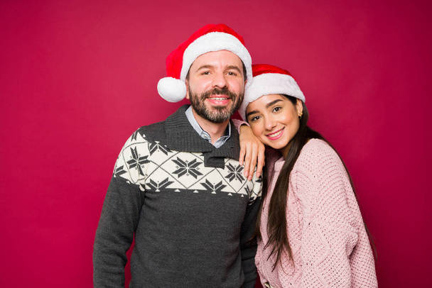 Attraktives glückliches Paar mit Weihnachtsmützen, lächelnd und umarmt, während es die Weihnachtsfeiertage genießt  - Foto, Bild