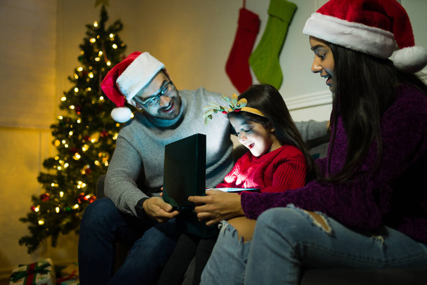 Aufgeregtes kleines Kind schaut überrascht beim Öffnen eines schönen Weihnachtsgeschenks mit ihren Eltern - Foto, Bild