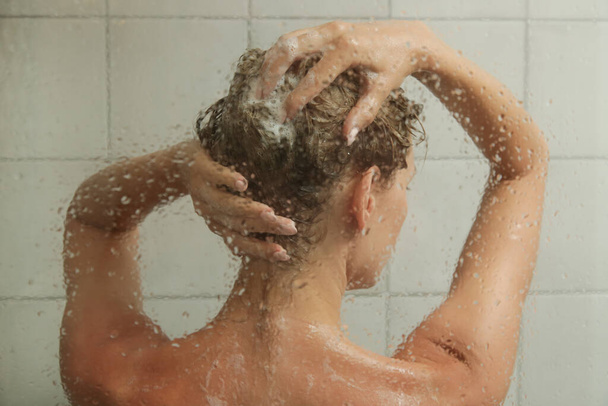Mladá žena se sprchuje a myje si vlasy ve sprchovém koutku. - Fotografie, Obrázek