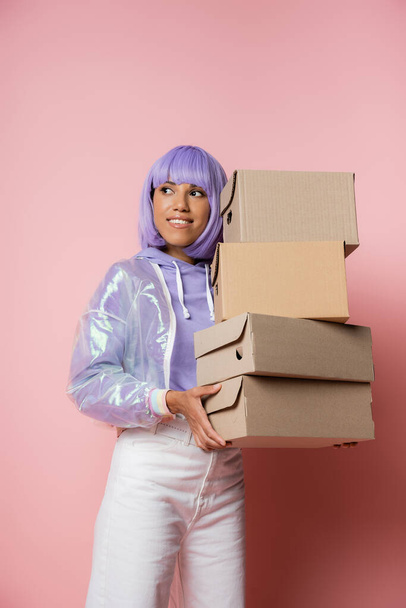 happy african american woman in purple wig holding carton boxes on pink  - Zdjęcie, obraz