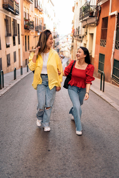 Trendy asian female friends talking while walking in the street and having fun. - 写真・画像