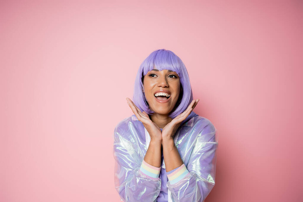 excited african american woman in purple wig and transparent jacket gesturing on pink  - Foto, Imagem