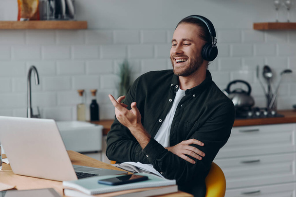 Cheerful young man in headphones talking and gesturing while having web conference from home - Photo, Image