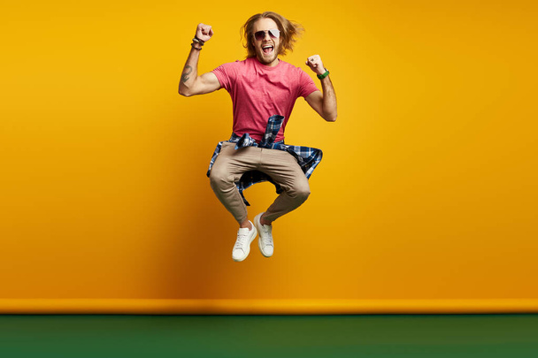 Excited young man gesturing while jumping against yellow background - Foto, immagini