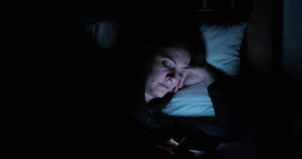 Young woman in bed with smartphone. Woman starring at cellphone device before going to bed - Footage, Video
