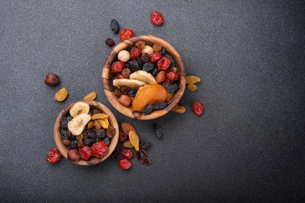 Widok z góry na drewniane miski z suszonymi owocami, jagodami i orzechami jako składnikiem smacznego i zdrowego posiłku na tle ciemnego betonu - Zdjęcie, obraz