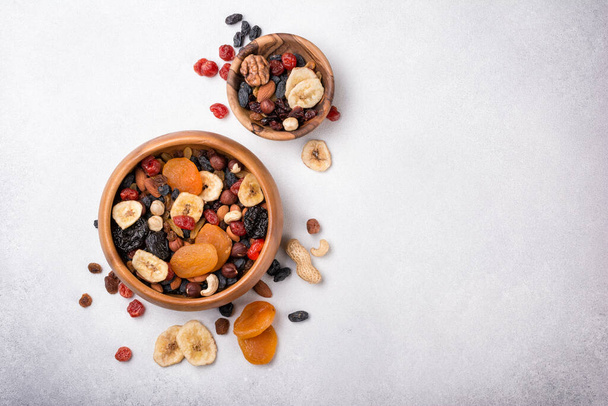 Top view of wooden bowls with dried fruit, berries and nuts as ingredient for tasty and healthy meal on grey concrete background - Fotó, kép