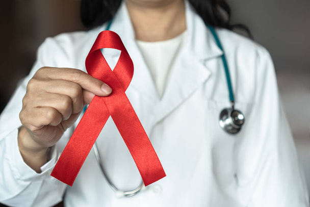 Welt-Aids-Tag und nationaler HIV-AIDS- und Alters-Bewusstseinsmonat mit roter Schleife an der Hand des Arztes oder Chirurgen  - Foto, Bild