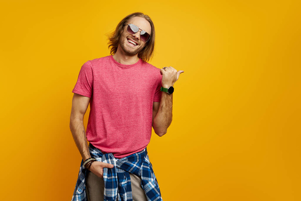 Happy young man pointing away while standing against yellow background - Фото, зображення