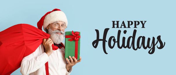 Санта-Клаус с подарком и сумкой на синем фоне. С праздником! - Фото, изображение