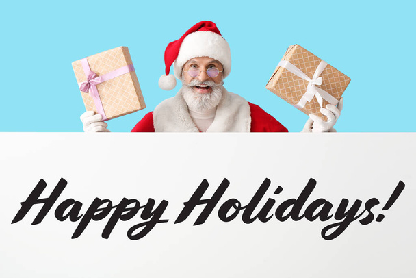 Weihnachtsmann mit Weihnachtsgeschenken und Poster mit Text HAPPY URIDAYS auf blauem Hintergrund - Foto, Bild