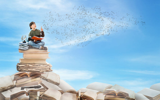 Mignon petit garçon assis sur la pile de livres dans le ciel bleu - Photo, image