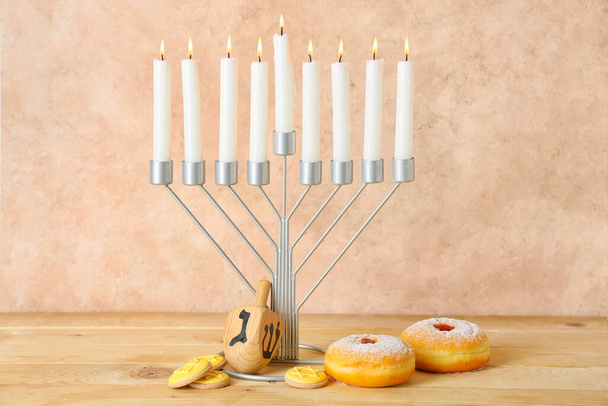 Menorah with candles, dreidel, donuts and cookies for Hanukkah celebration on wooden table against color background - Фото, изображение