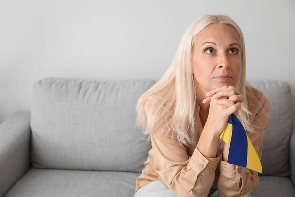 Mature woman with flag of Ukraine praying at home - Foto, imagen
