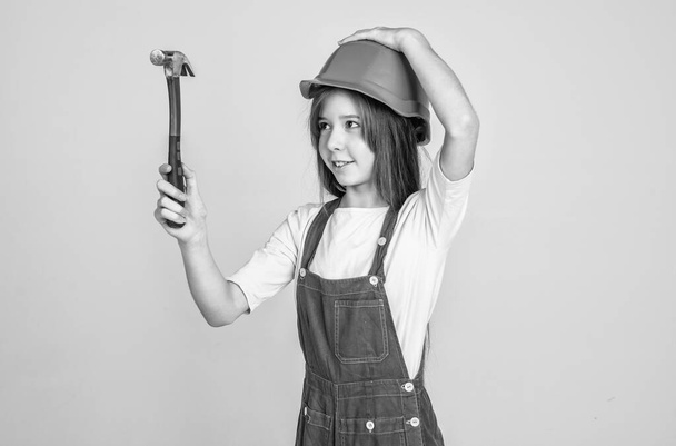 teen girl laborer in protective helmet and uniform on grey background use hammer, worker. - Photo, image
