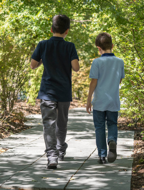 Chłopcy bracia lub przyjaciele w luźnych ubraniach spacerujący za drzewami i cieniami. Koncepcja czasu razem - Zdjęcie, obraz