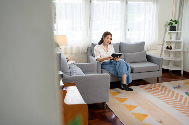 Young asian woman using tablet on sofa in living room	 - Photo, image