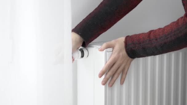 Человек касается холодного радиатора домашнего обогревателя своими замороженными руками и увеличивает мощность нагрева на максимальное значение. Ограничение потребления энергии в отопительный сезон. Энергетический кризис. - Кадры, видео