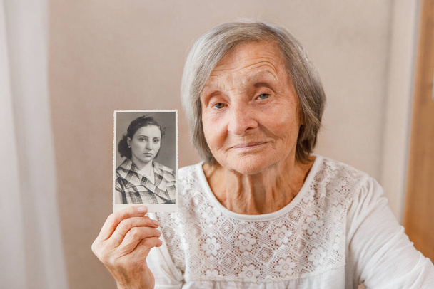 Starsza kobieta trzyma zdjęcie ich młodości. Wspomnienia, nostalgia, koncepcja czasu Zdjęcie zostało zrobione w 1958 roku - Zdjęcie, obraz