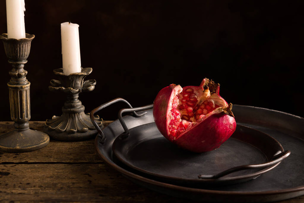 Still life on wooden table with antique plates and a pomegranate cut open. - Foto, Imagem