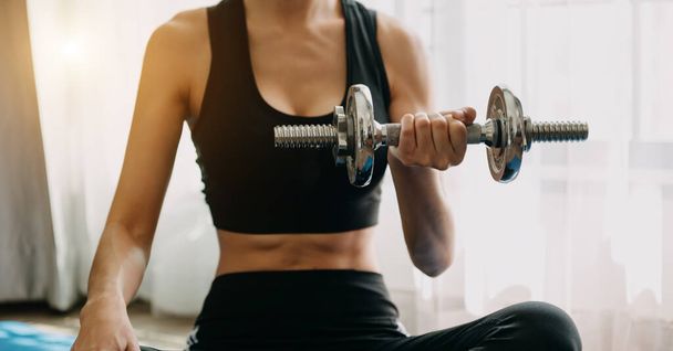 Determined woman losing weight at home and exercising with dumbbells. Sport and recreation concept. Beautiful woman in sportswear - Φωτογραφία, εικόνα